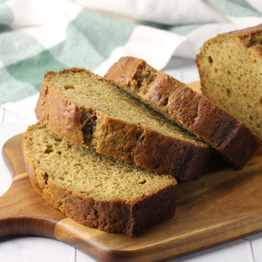 Slices of applesauce zucchini bread on a wooden cutting board.