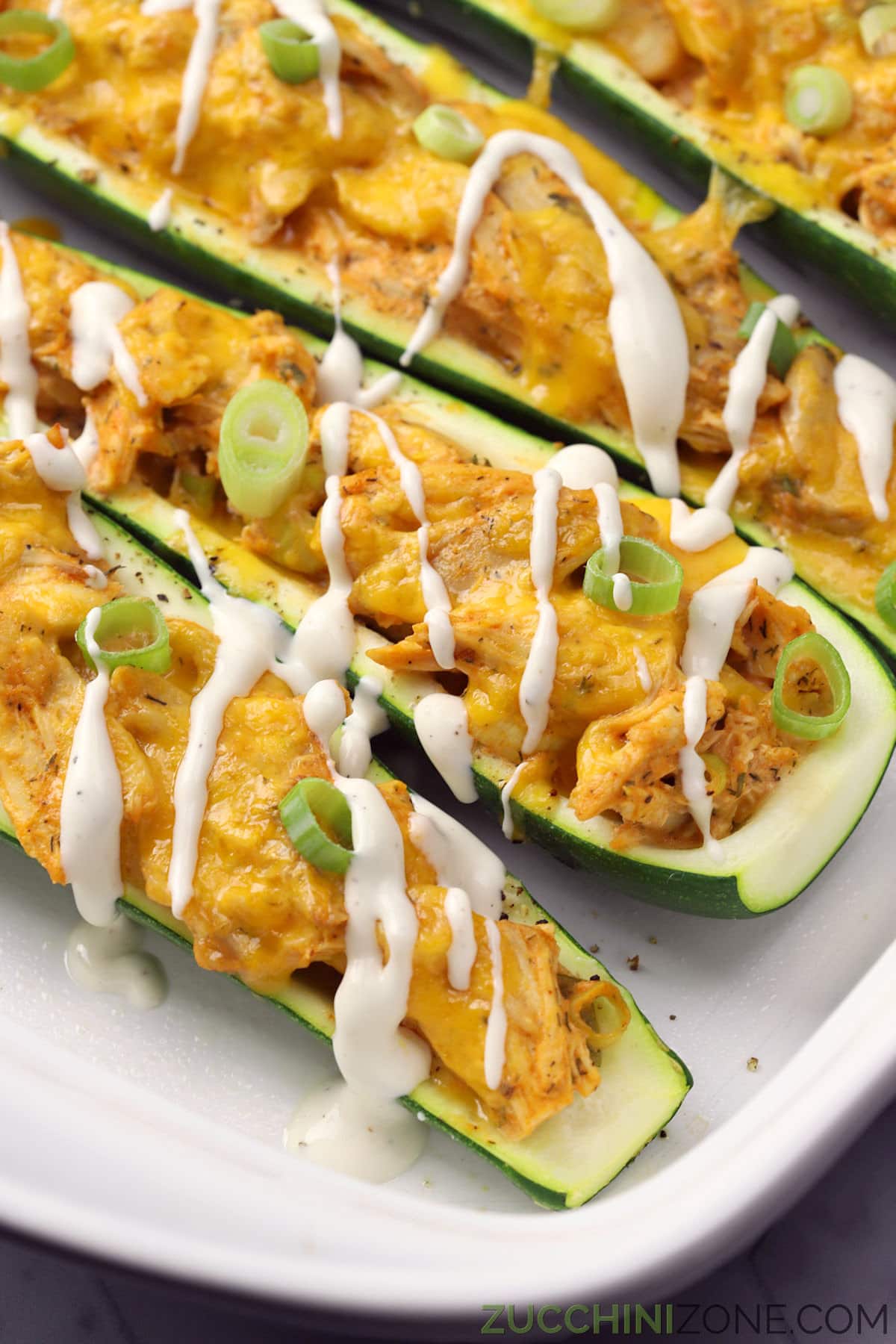 Buffalo chicken zucchini boats drizzled with ranch dressing in a white casserole dish.