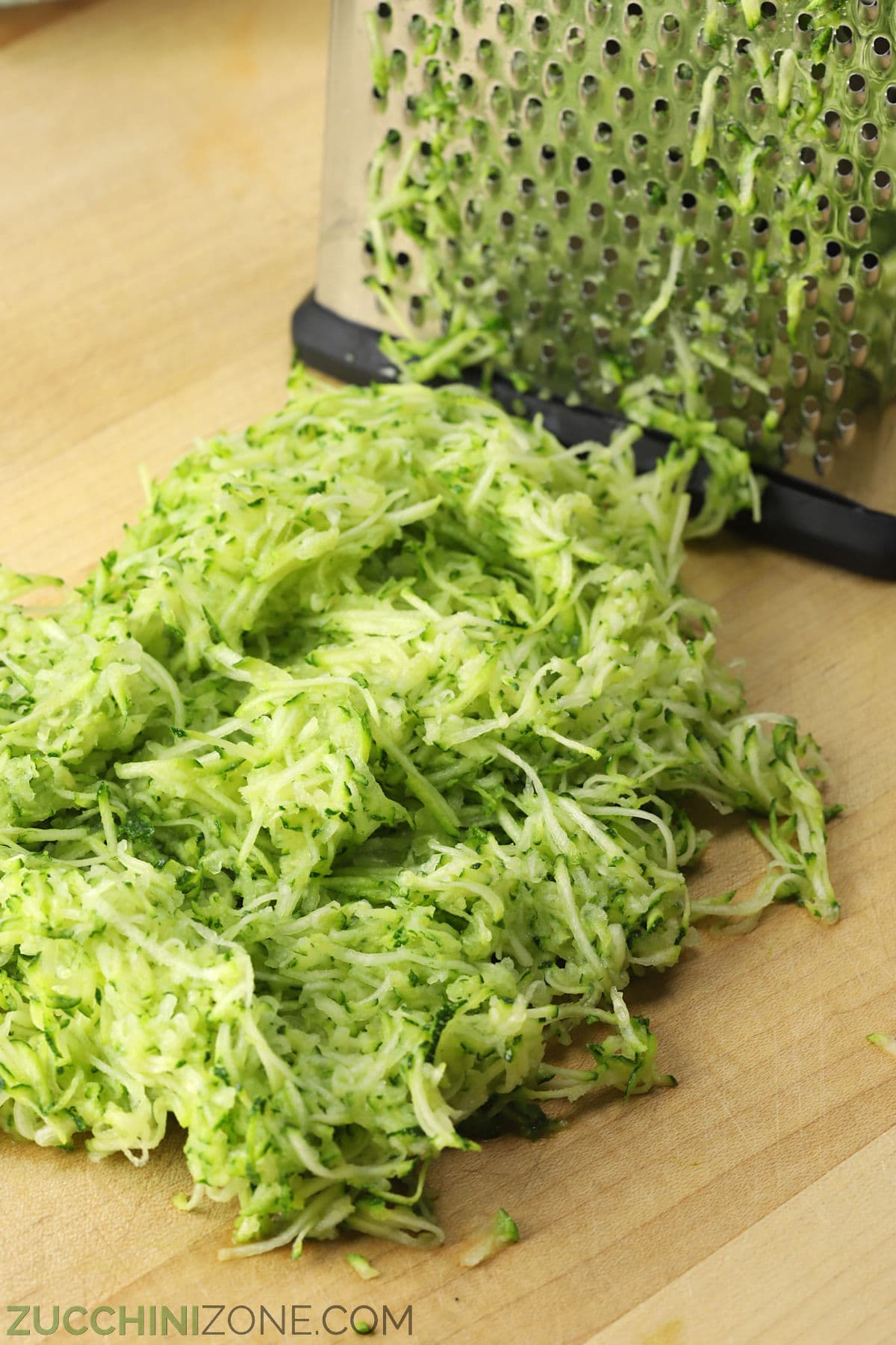 Finely grated zucchini on a wooden cutting board.