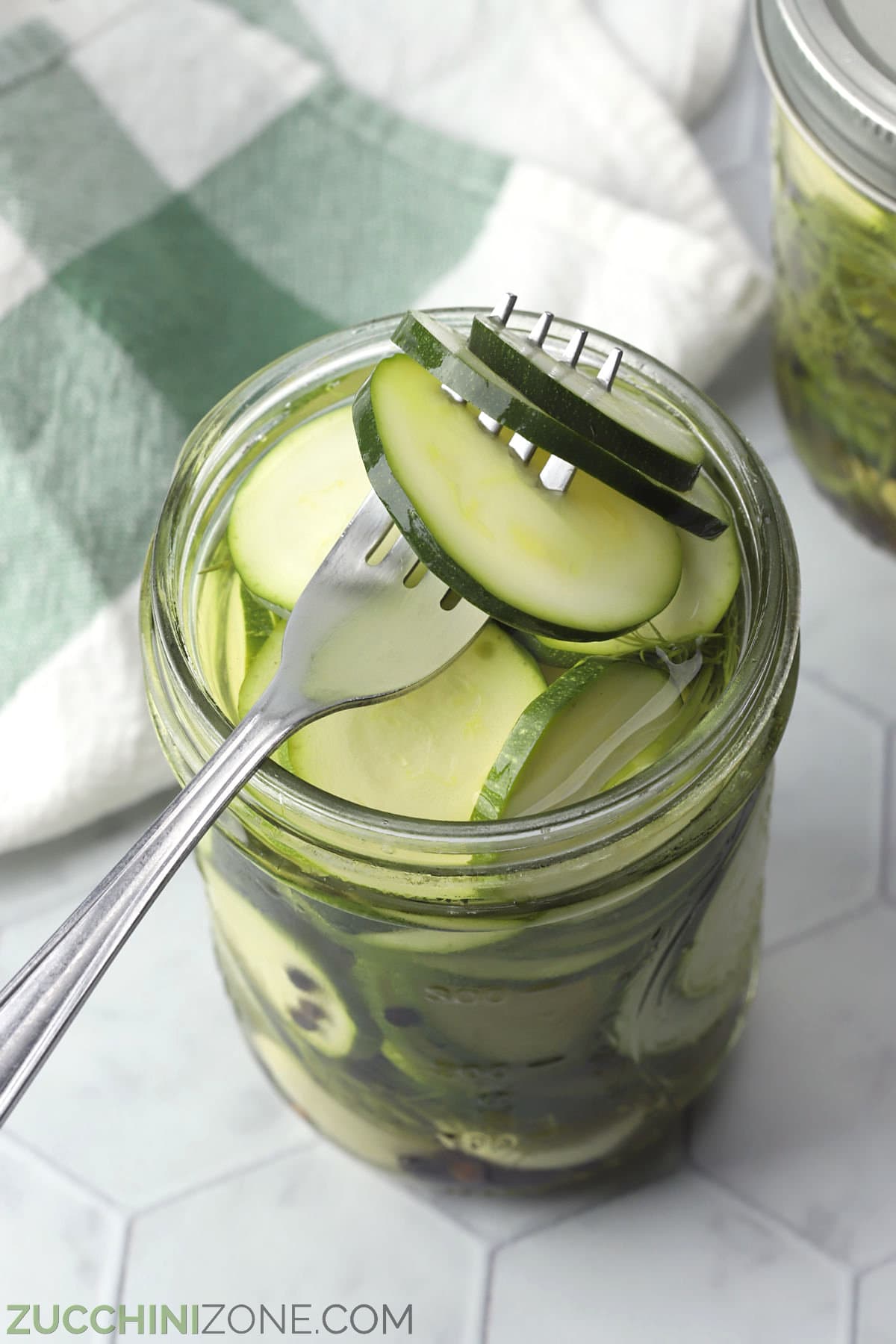 A fork piercing through zucchini pickles in a glass jar.