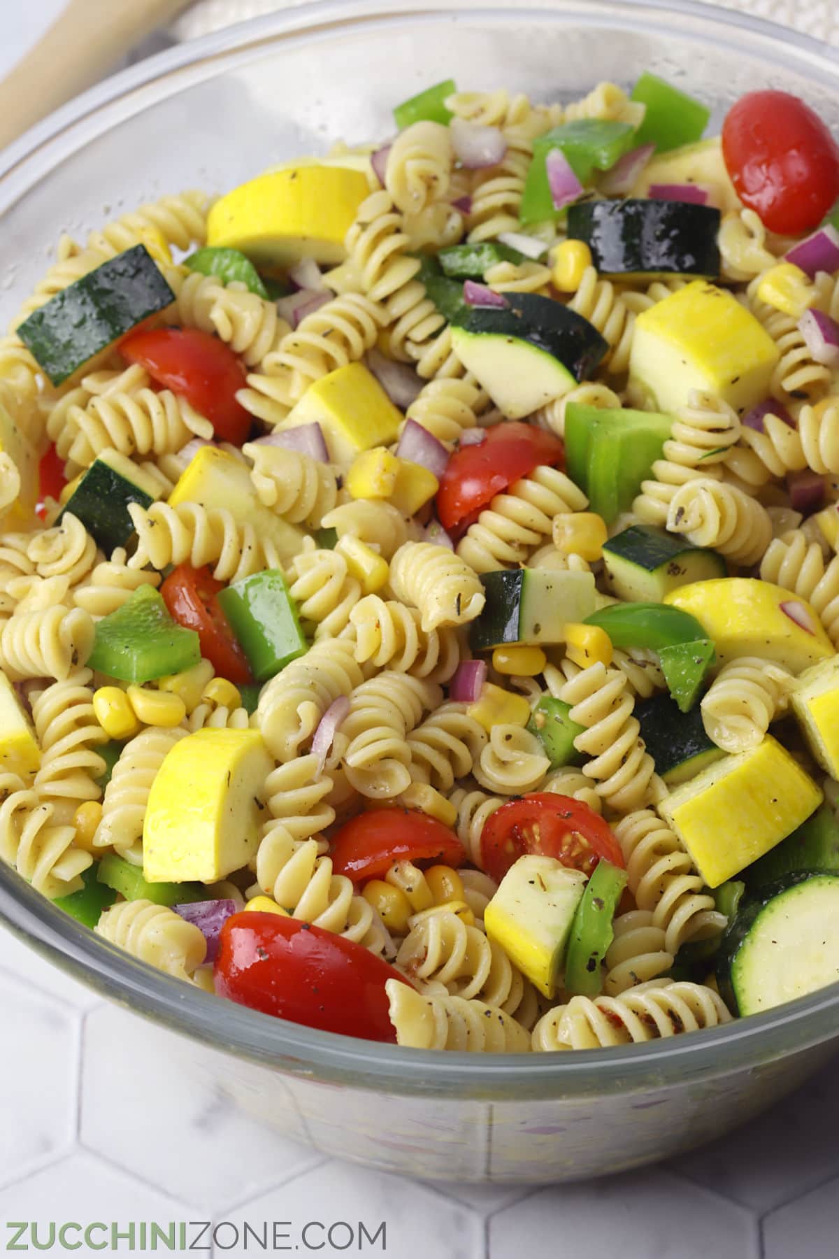 A tossed summer vegetable pasta salad in a glass bowl.
