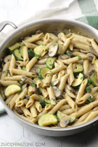 Saute pan filled with pasta, zucchini, and mushrooms in a cream sauce.