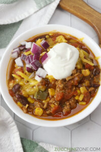 A white bowl filled with chili topped with sour cream and cheese.
