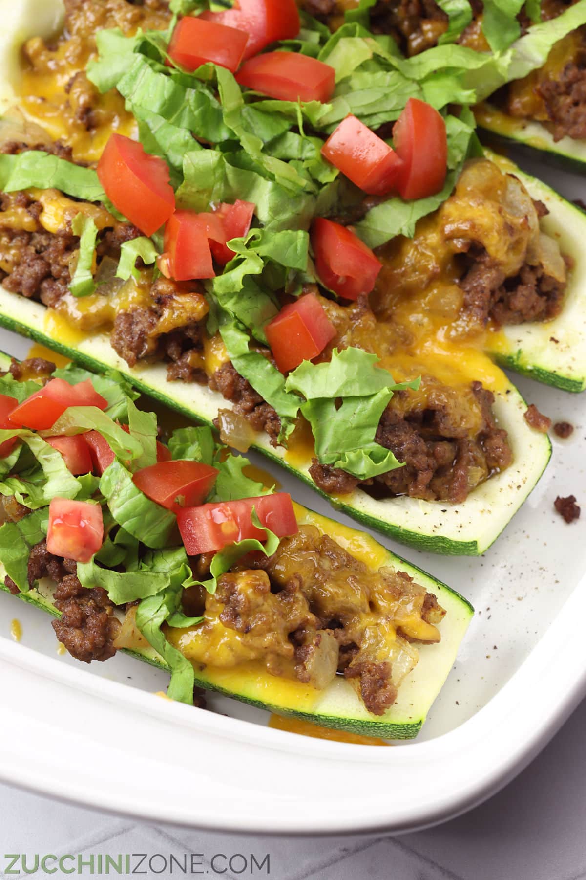 Close up of cheeseburger zucchini boats topped with lettuce and tomato.