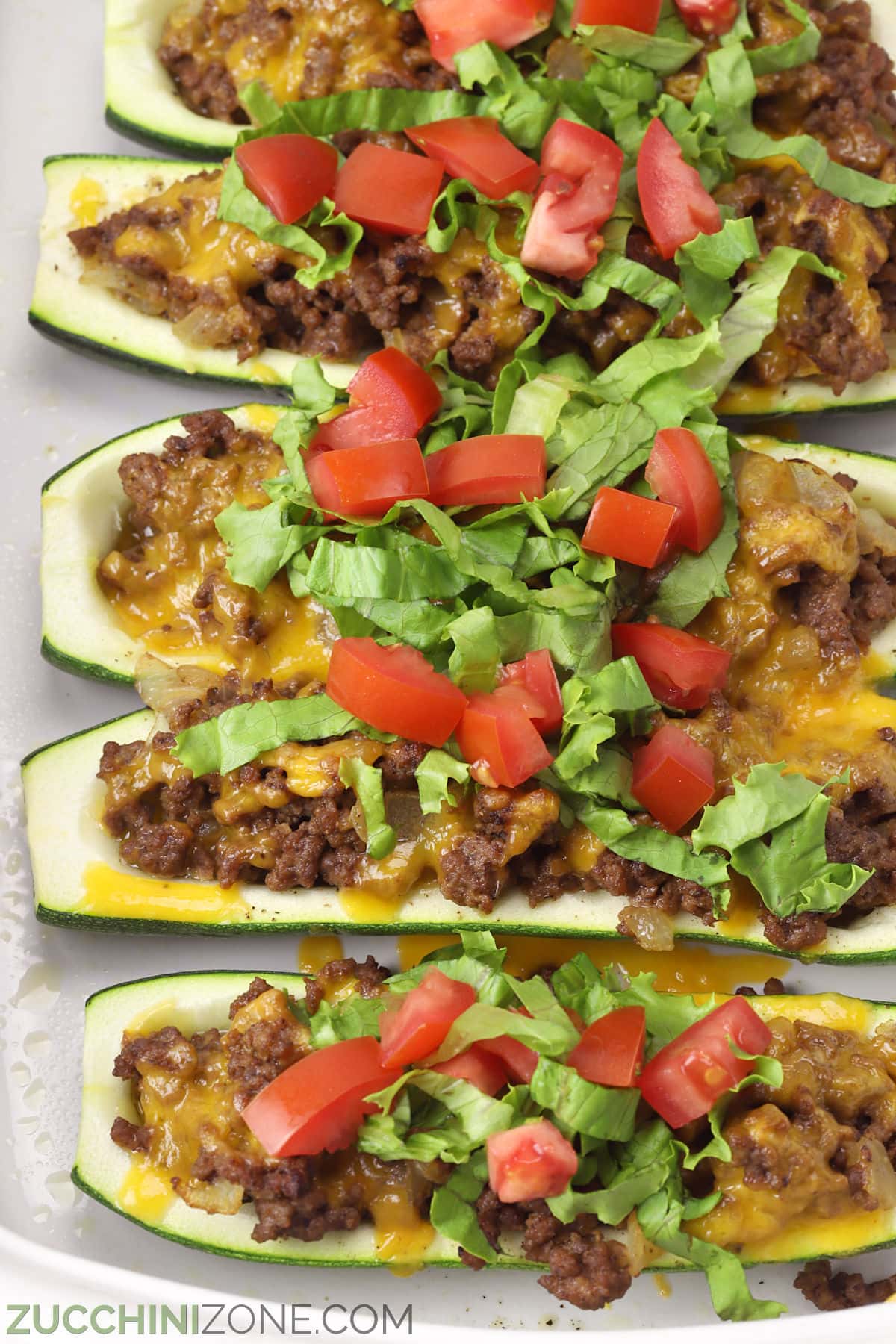 Cheeseburger zucchini boats lined up in a white casserole dish.