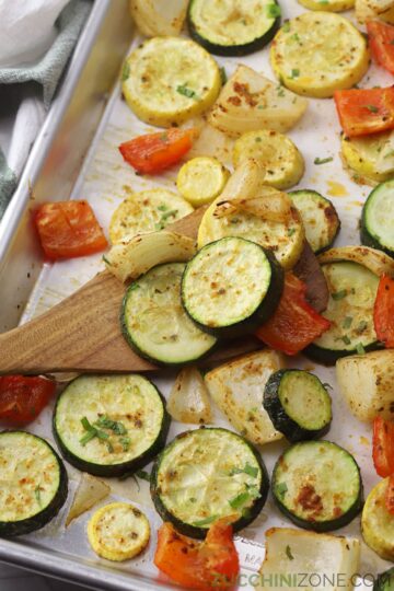 Spatula scooping roasted vegetables from a sheet pan.