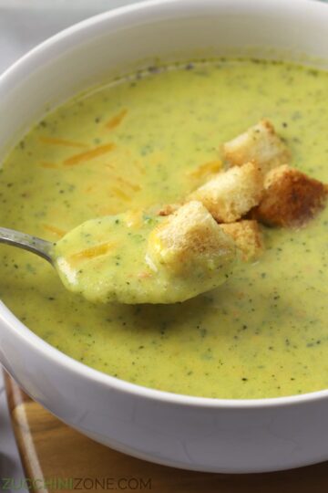 Spoon of broccoli cheddar zucchini soup with croutons on top.