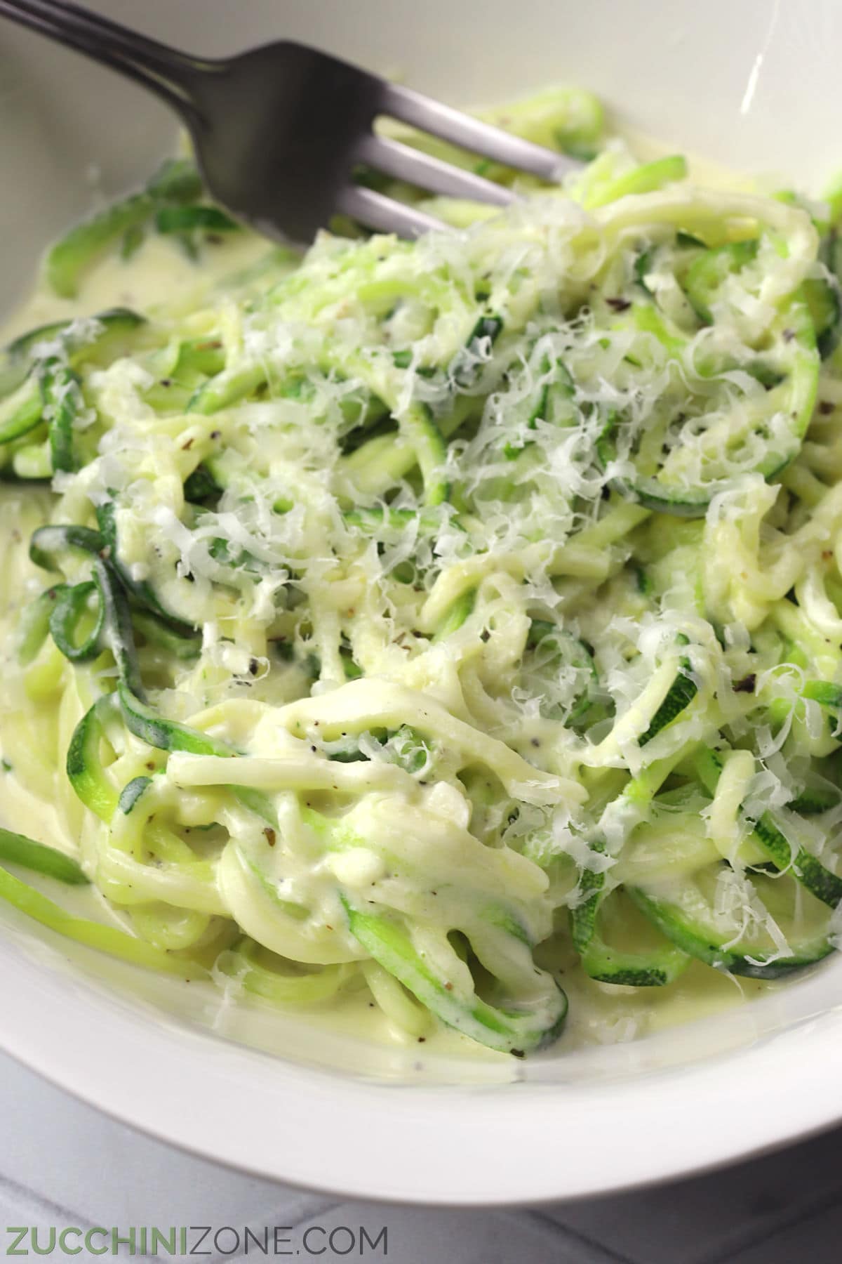 Close up of zucchini noodles covered in alfredo sauce and shredded parmesan.