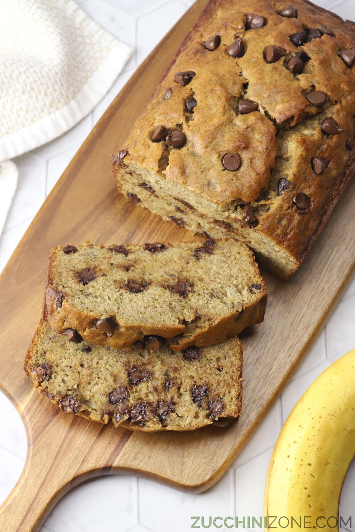 A loaf of chocolate chip banana zucchini bread on a wooden cutting board.