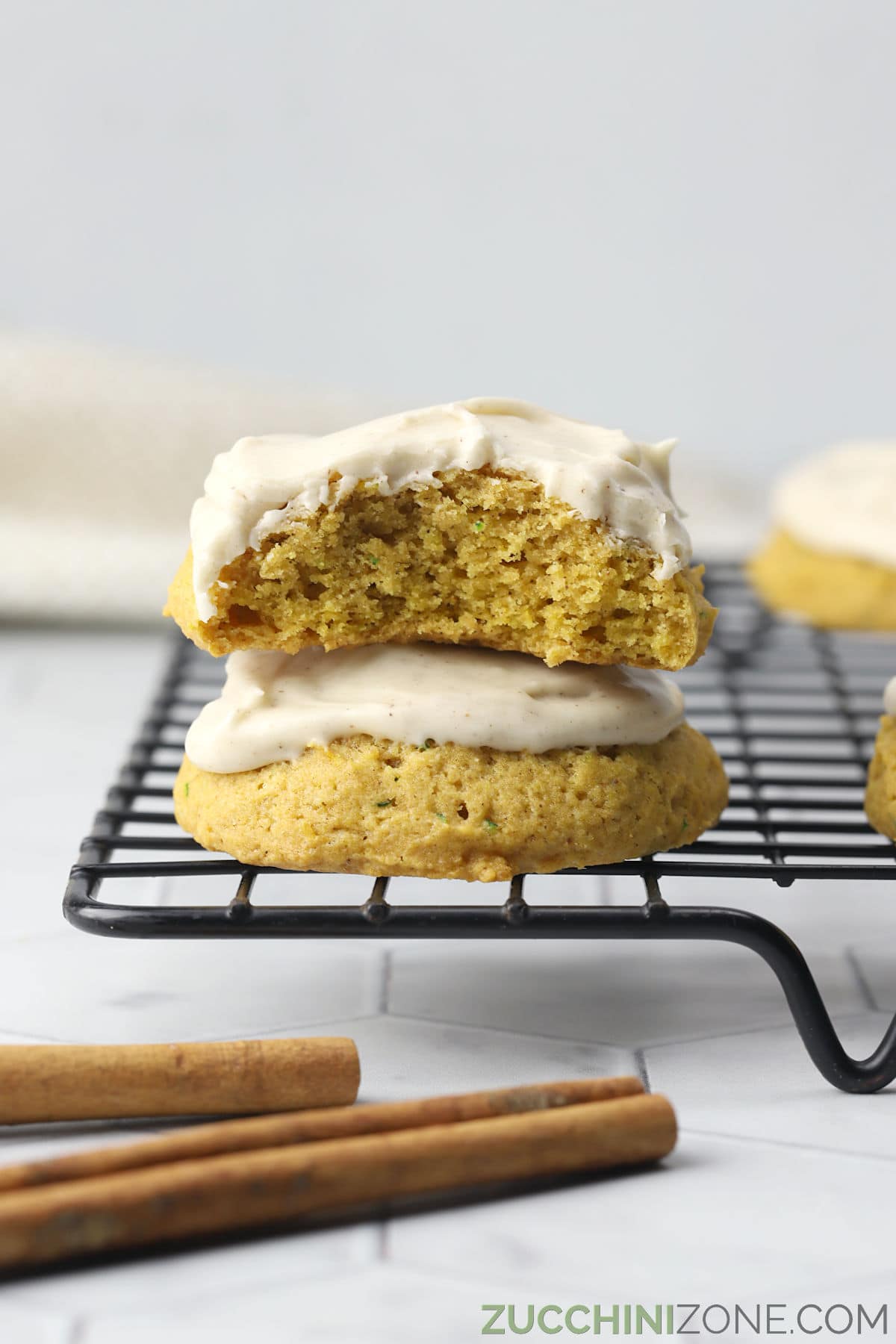 Two pumpkin zucchini cookies stacked on a cooling rack, one with a bite missing.