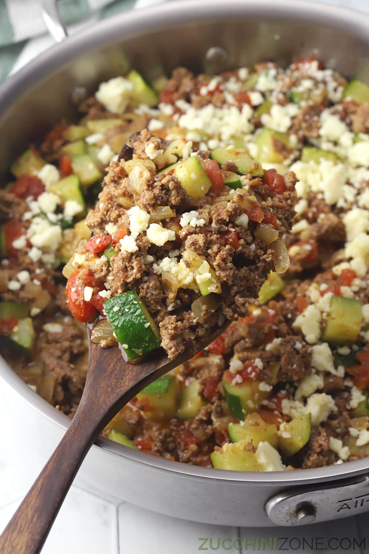 A wooden spatula filled with ground beef, zucchini, and tomatoes.