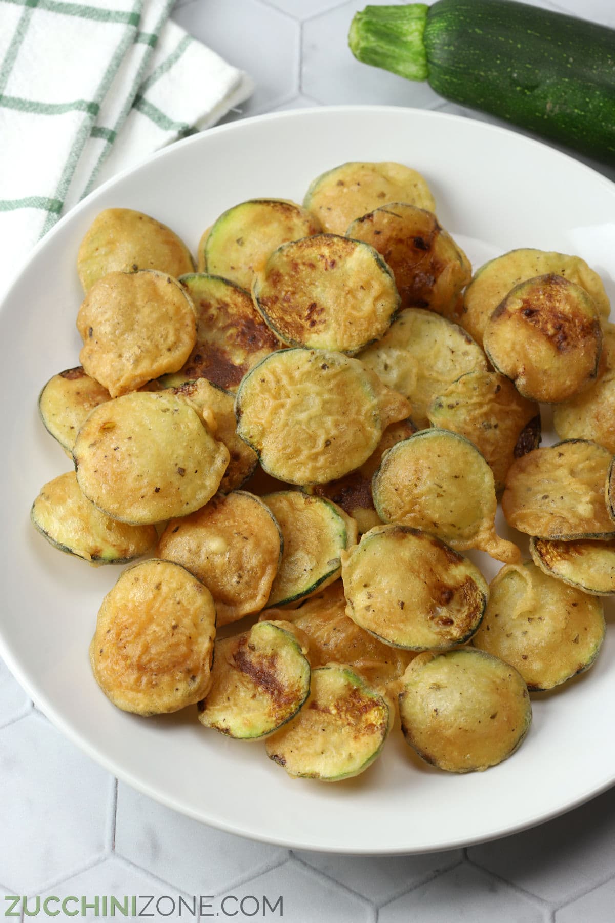 A white serving plate filled with crispy Greek fried zucchini chips.