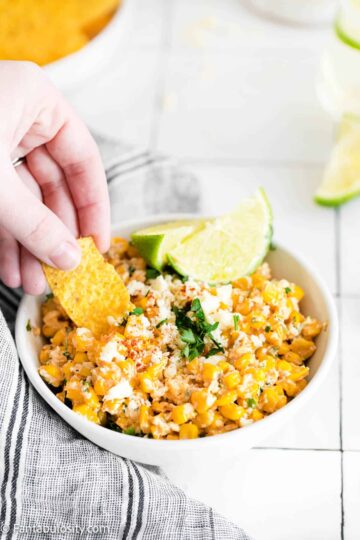 Bowl of elote dip with lime wedges.