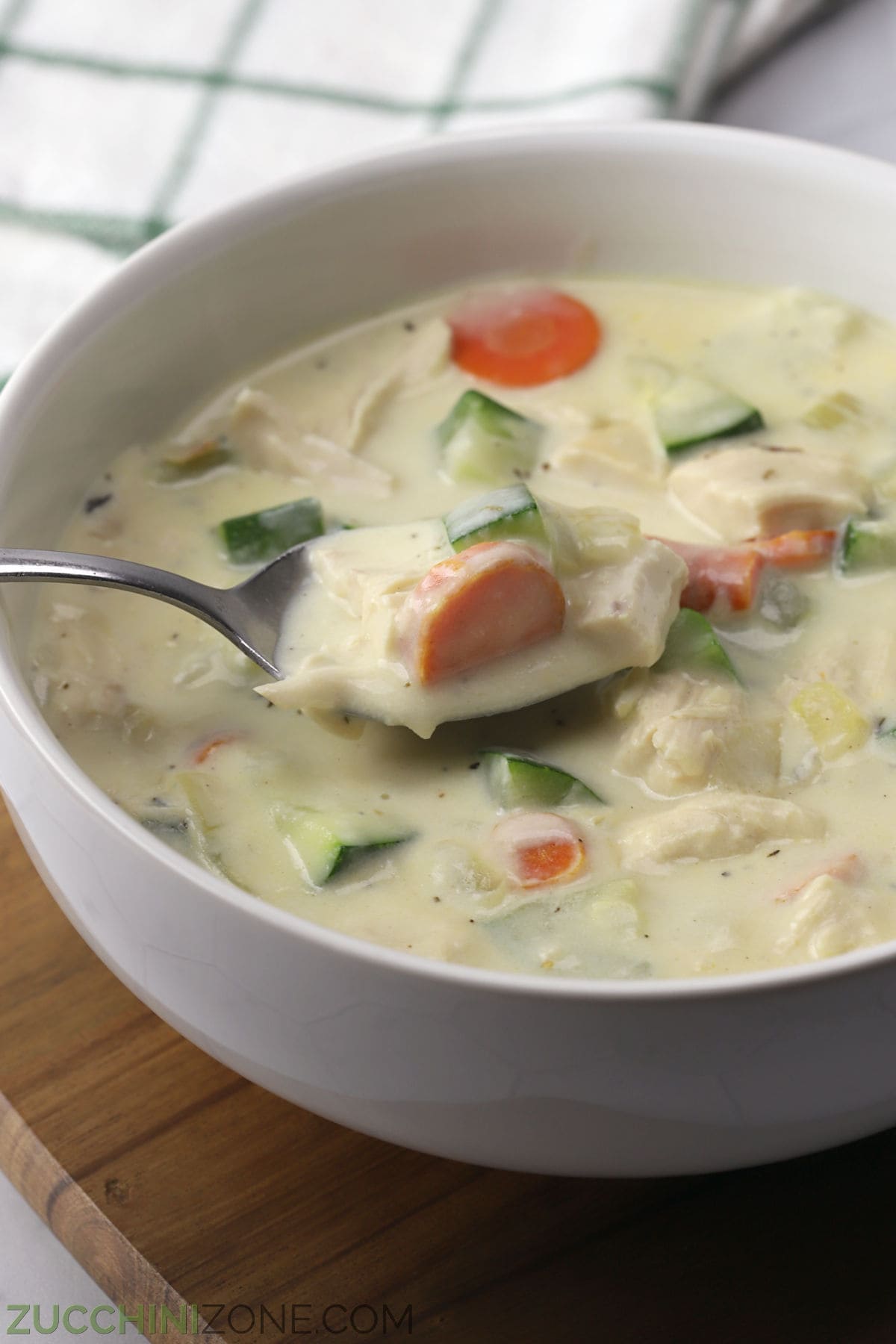Closeup of creamy chicken vegetable soup in a bowl with a metal spoon.