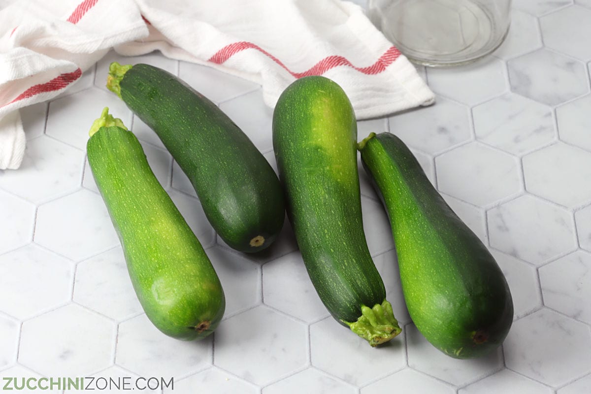 Four zucchini on a countertop with a kitchen towel.