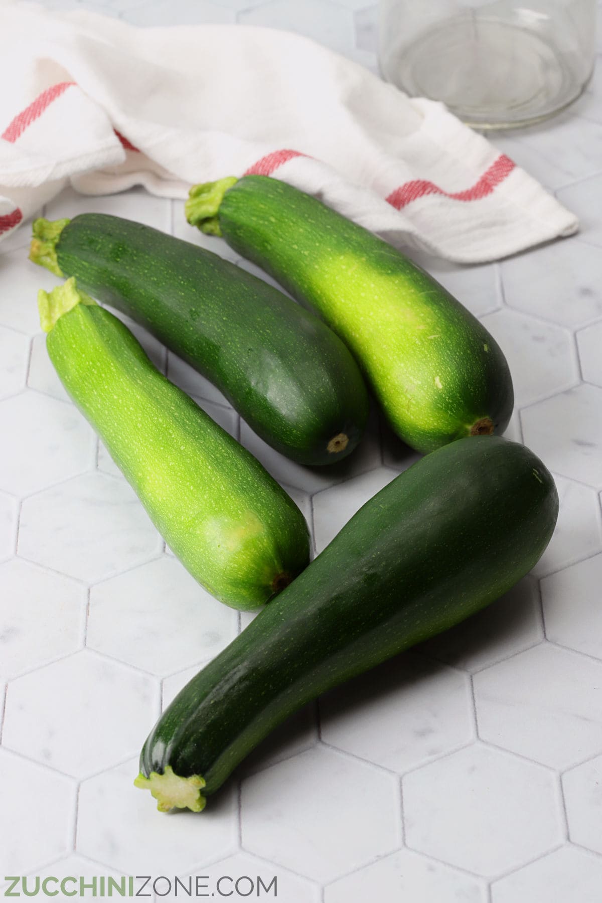 Four zucchini on a countertop with a kitchen towel.