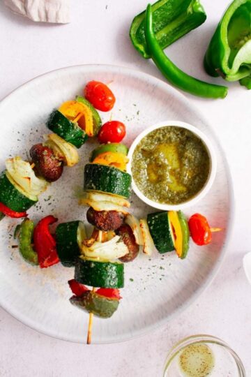 Skewers of vegetables on a plate with a dipping sauce.