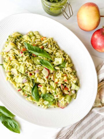 An oval serving bowl filled with pesto orzo salad.