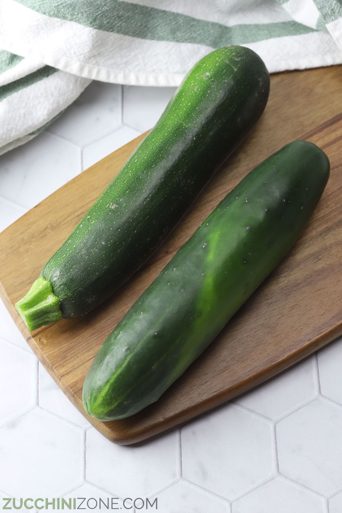 Zucchini and cucumber laying on a wooden cutting board.