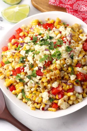 A white bowl filled with corn salad topped with cilantro and crumbled cheese.