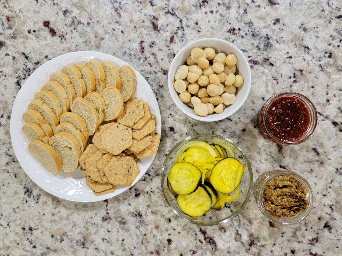 Crackers, nuts, pickles, and jams in containers ready to add to a charcuterie board.