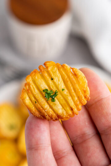 A small potato disc garnished with parsley and held on finger tips.