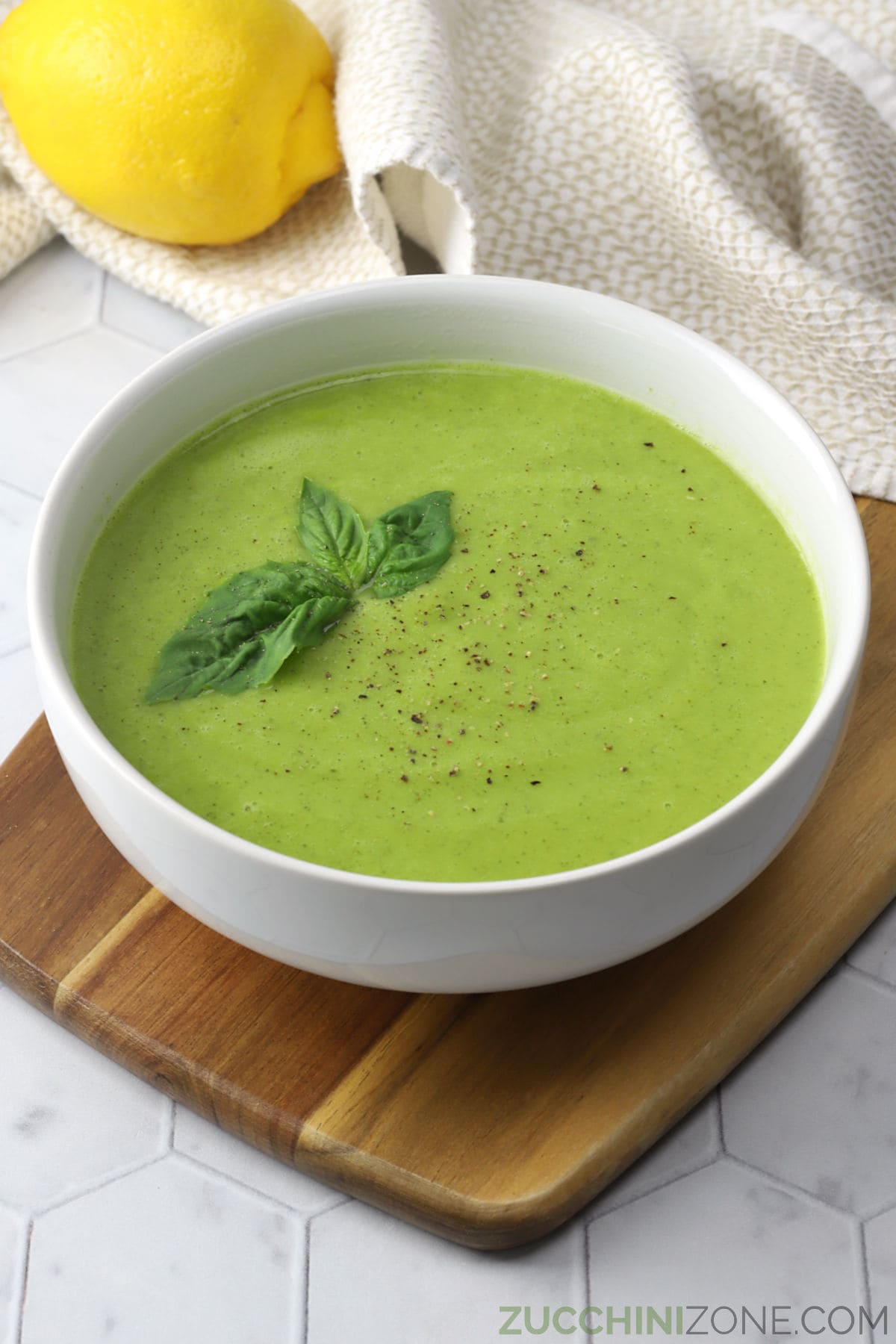 A white bowl filled with vibrant green soup and fresh basil leaves.