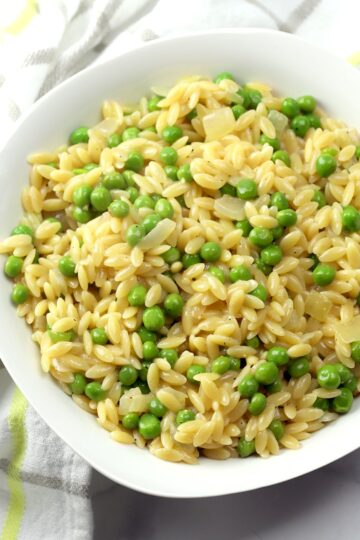 Orzo and green peas in a white bowl.