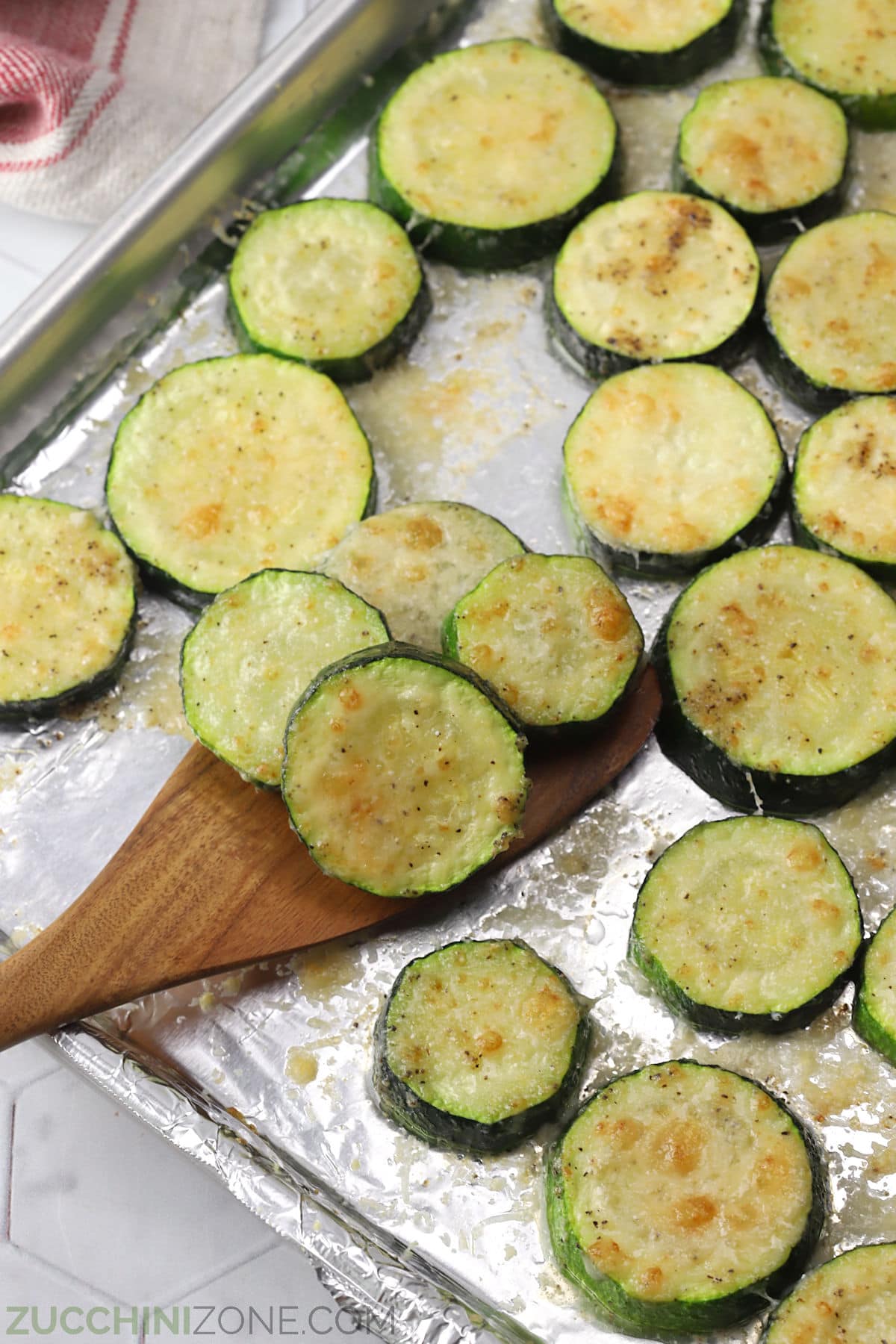 A wooden spatula scooping broiled zucchini from a sheet pan.