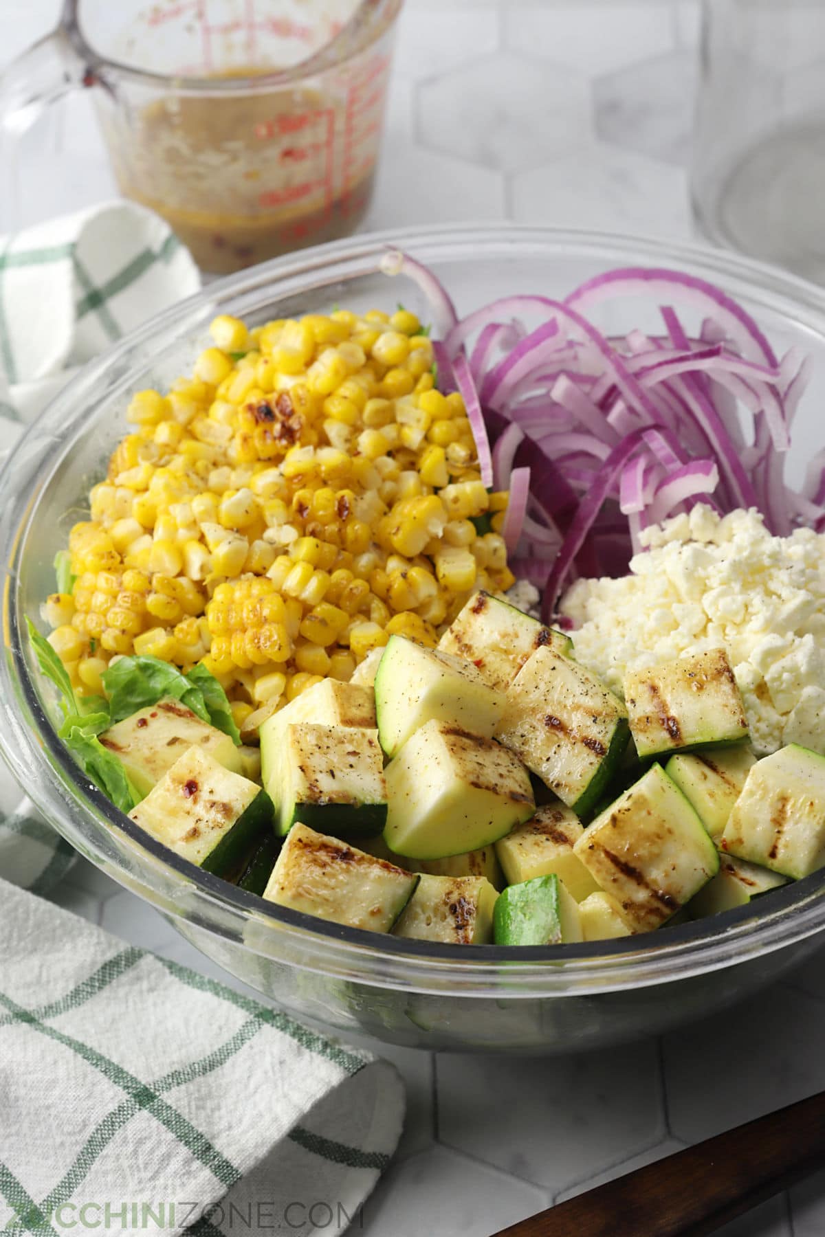 A glass bowl filled with grilled zucchini salad ingredients.