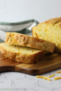 Close up of slices of cheese zucchini bread on a wooden serving board.