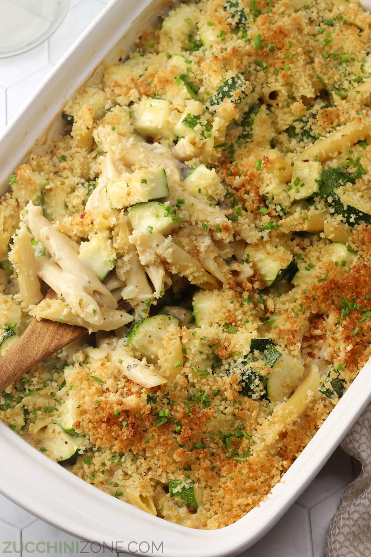 Close up of baked zucchini pasta being scooped with a wooden spoon.