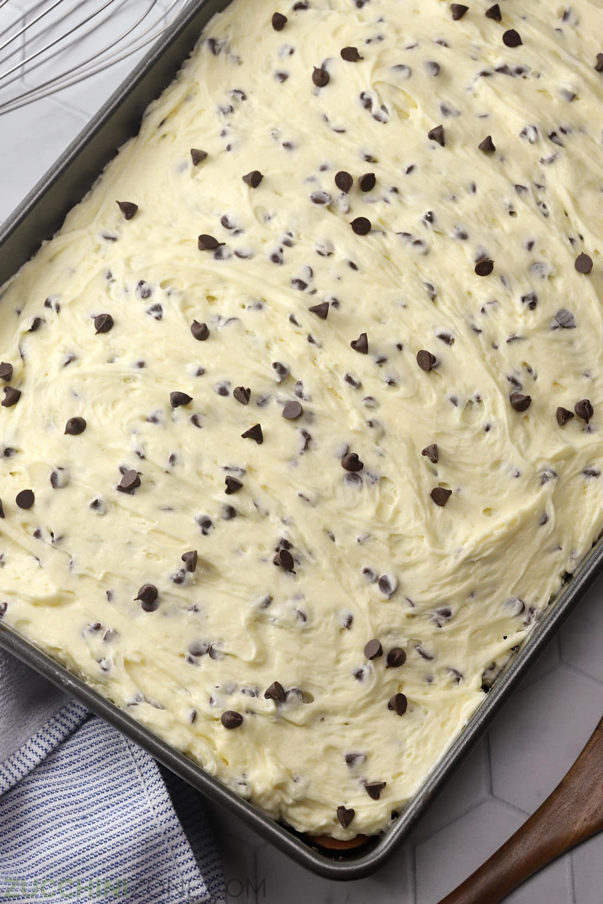 A chocolate chip zucchini cake with frosting in a 9x13 baking pan.