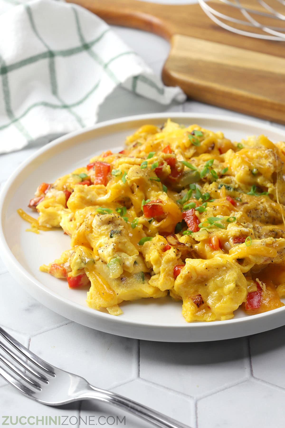 Close up of scrambled eggs and veggies topped with melted cheese on a white plate.