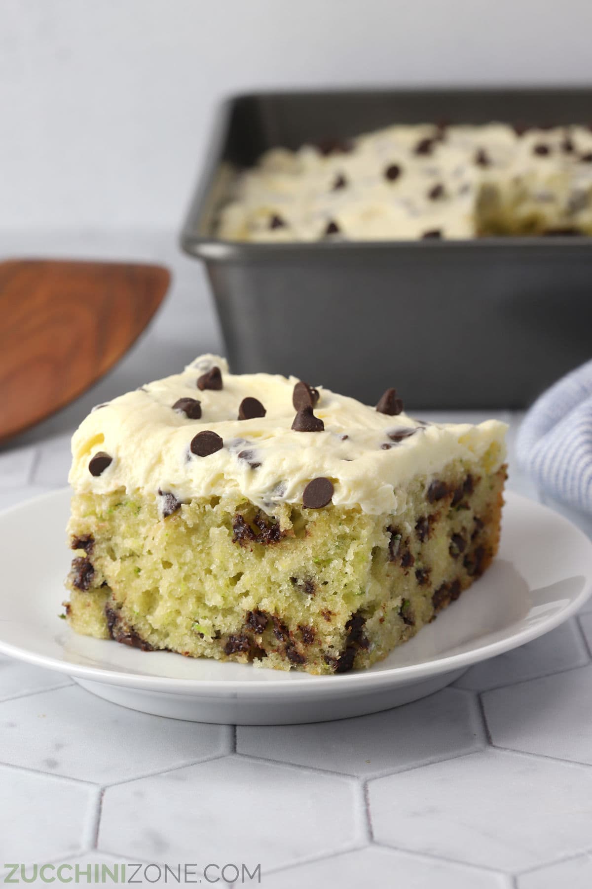 A slice of chocolate chip zucchini cake on a white serving plate.