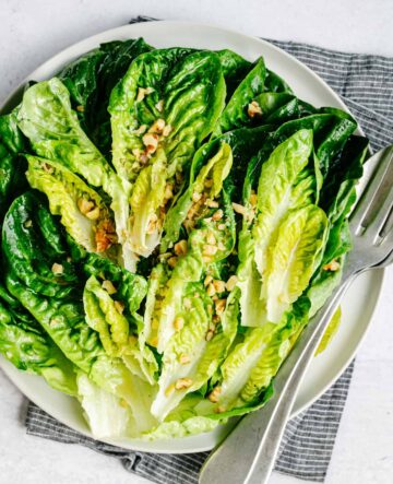 A white plate of salad and nuts.