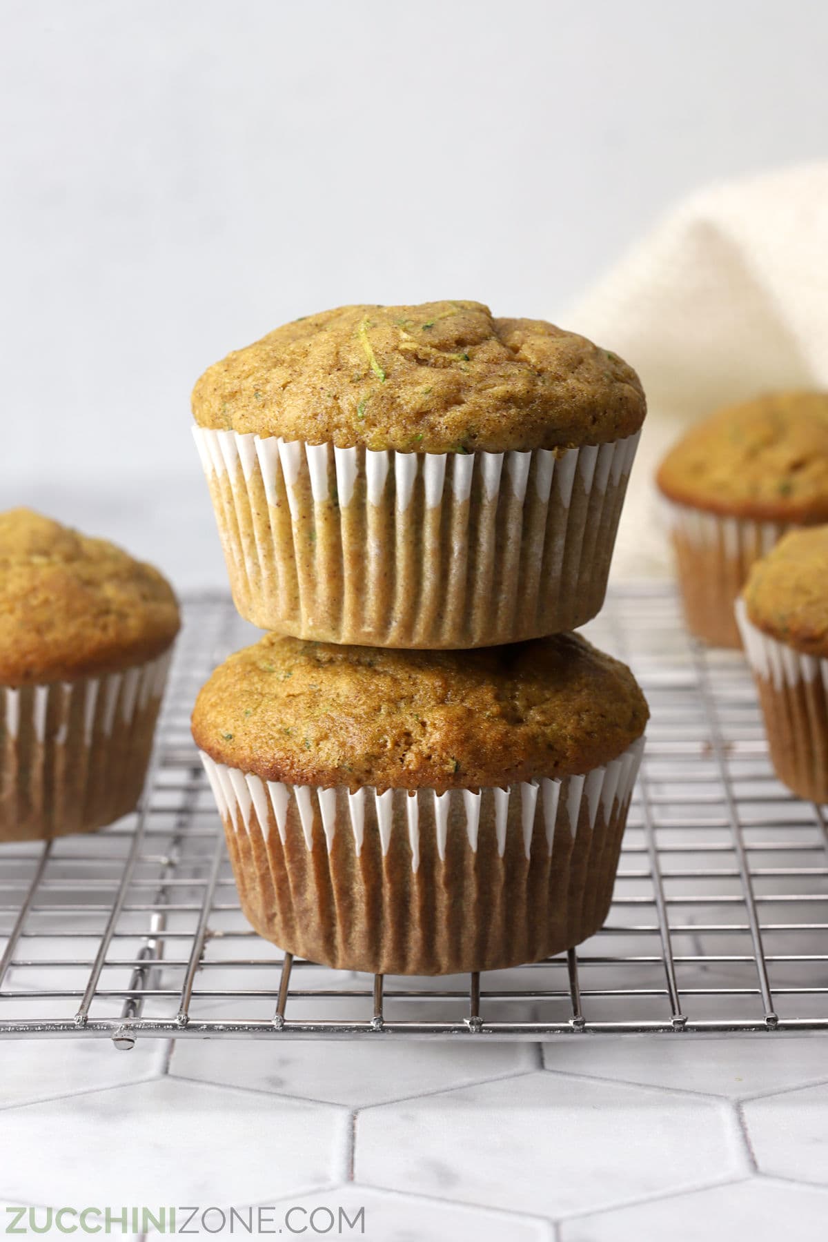 Two gluten-free zucchini muffins with paper wrapped stacked on a cooling rack.