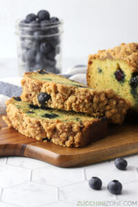 Slices of blueberry streusel zucchini bread on a cutting board.