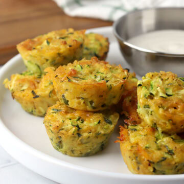 Cheesy zucchini bites stacked on a plate.