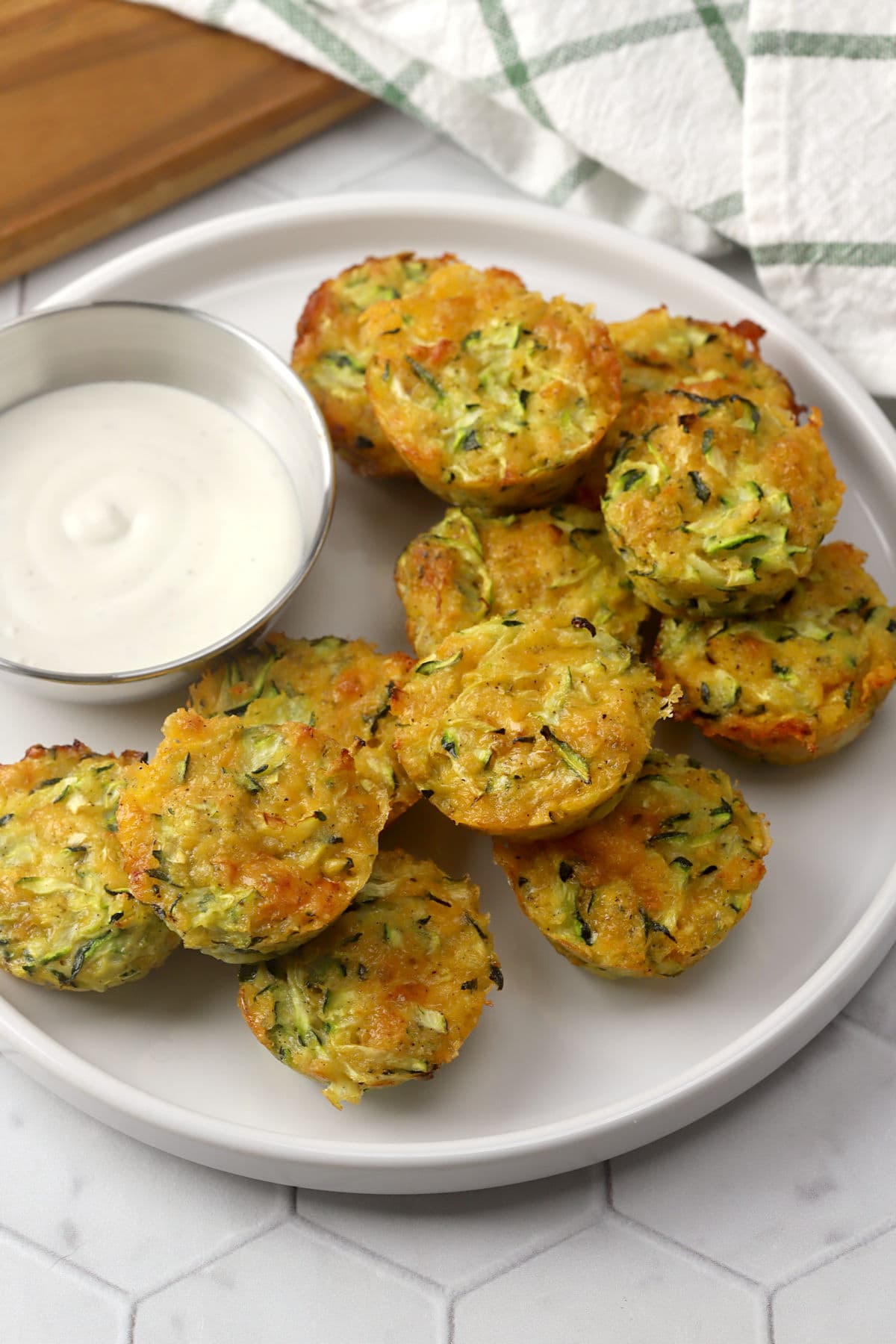 A crescent of zucchini bites arranged around a dish of dipping sauce.