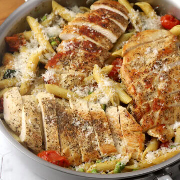 A pan of pasta and vegetables with sliced chicken breast on top.
