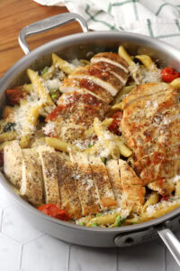 A pan of pasta and vegetables with sliced chicken breast on top.