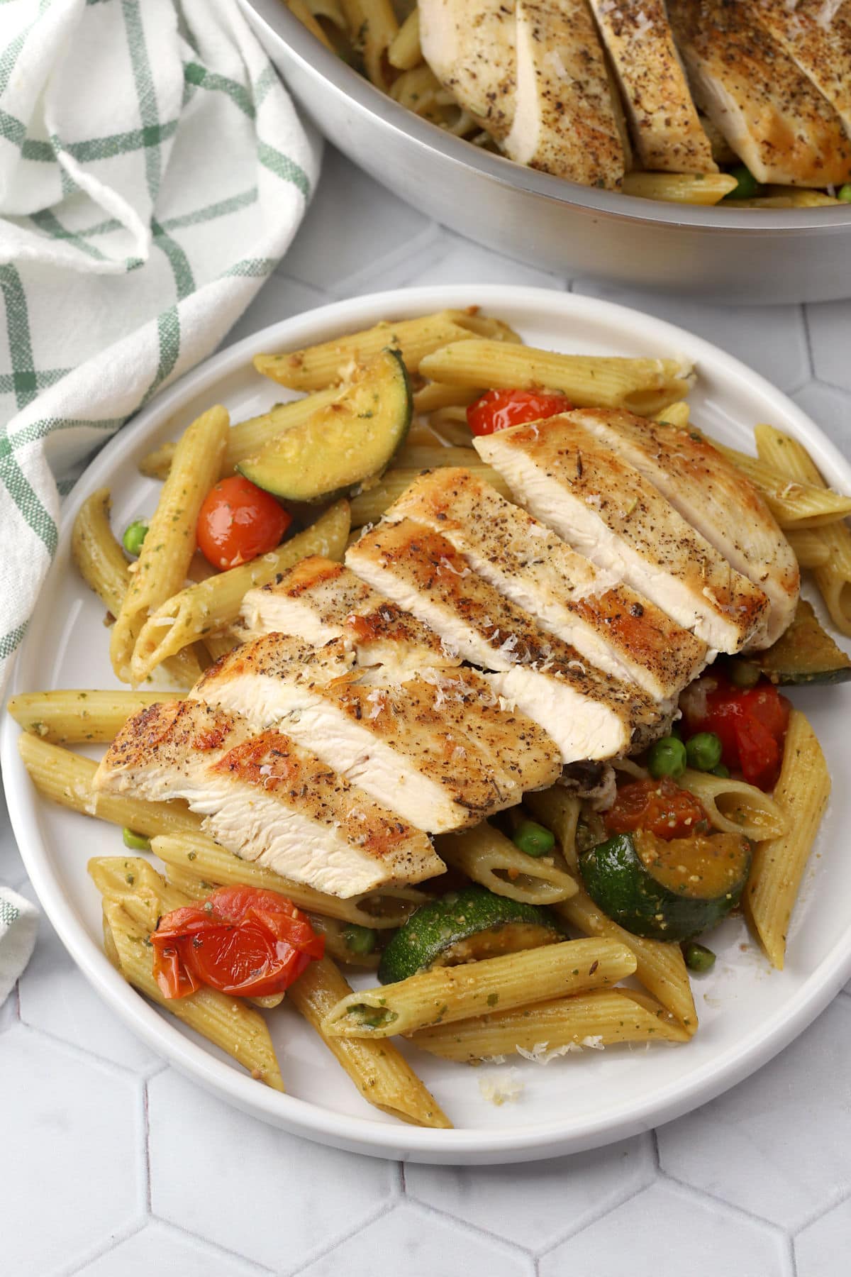 Pasta and vegetables on a plate with sliced chicken breast on top.