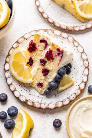 A slice of layered cake garnished with lemon and blueberries.